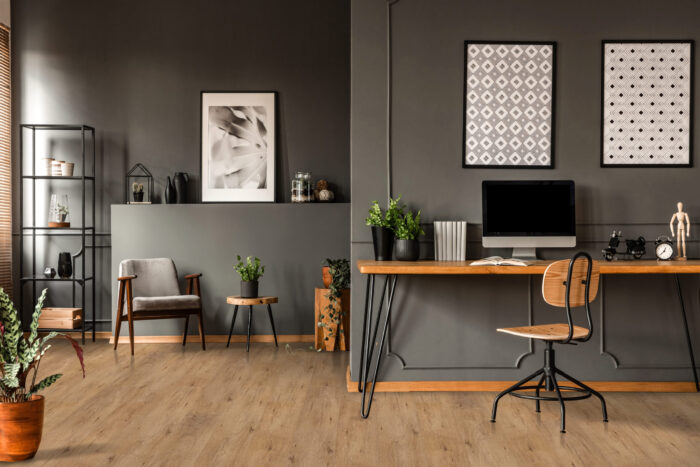 Modern home office with rustic hardwood flooring in a warm brown tone, featuring a minimalist wooden desk, vintage chair, and dark accent walls. Premium hardwood floors from Rustic Wood Floors Supply.