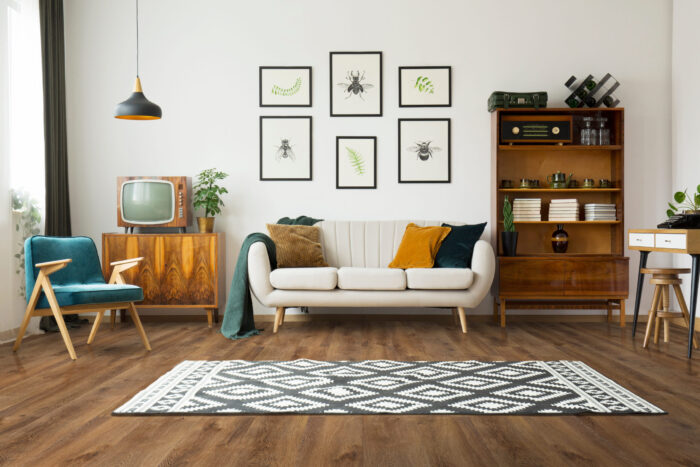 Rustic wide plank hardwood flooring in a warm brown tone, showcasing a living room interior with mid-century modern furniture, a patterned rug, and white walls. Ideal for demonstrating the aesthetic of installing rustic wood floors from Rustic Wood Floors Supply