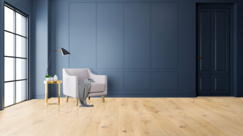 Light-toned, wide plank hardwood flooring from Rustic Wood Floors Supply, showcasing a modern room with blue paneled walls, a white armchair, and a black framed window, highlighting the flooring's ability to brighten a space
