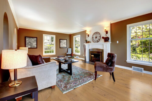 Light oak wide plank hardwood flooring from Rustic Wood Floors Supply in a traditional living room, showcasing warm brown walls, a white fireplace, and comfortable seating, emphasizing the flooring's ability to brighten and expand a space.