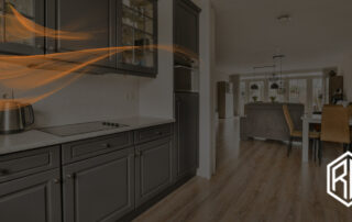 Modern open-plan kitchen and dining area featuring gray cabinetry, a kettle on the countertop, and wood-look plank flooring, overlaid with translucent orange swoosh graphics and the text ‘6 kitchen Flooring trends 2025,’ plus an RW logo in the lower right.