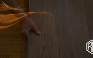 Hand installing a plank of the best hardwood flooring for high-traffic areas with artistic orange light streaks and RW logo in the corner.