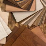 A variety of wood and laminate flooring samples in different colors and grains are fanned out on a wooden surface, showing different options for wholesale wood flooring supplies.